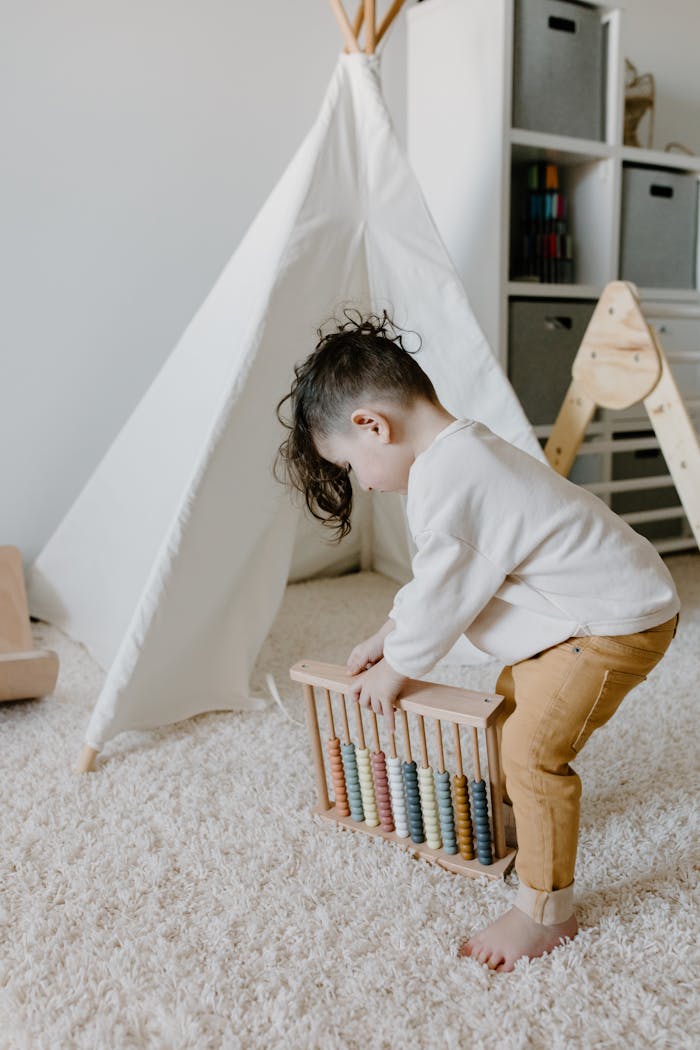 A young child plays with an abacus in a cozy indoor setting with a teepee and plush carpet.
